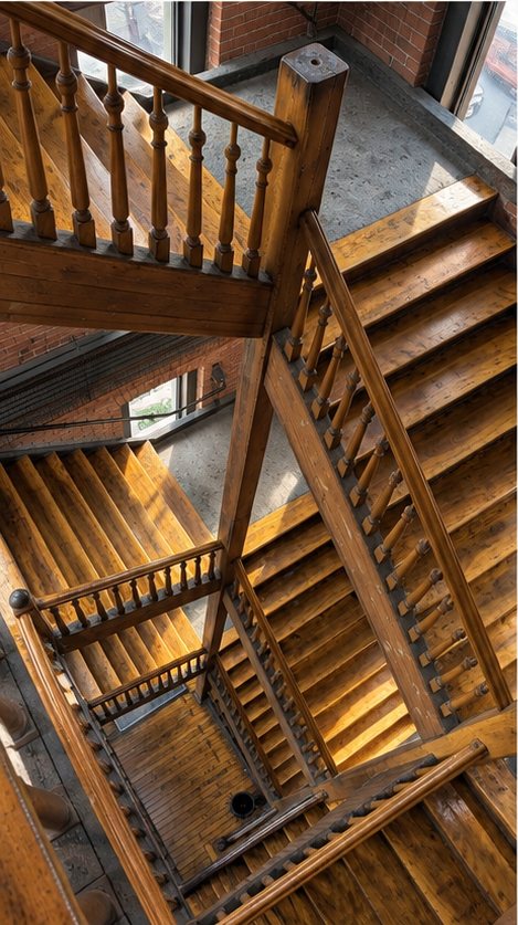 Cage d'escalier de bois vernis vue d'en haut, volées et rampes tournées s'entrecroisant sur plusieurs étages.