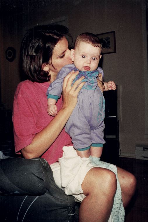 Josée embrassant un bébé en pyjama mauve qu'elle tient à bout de bras.