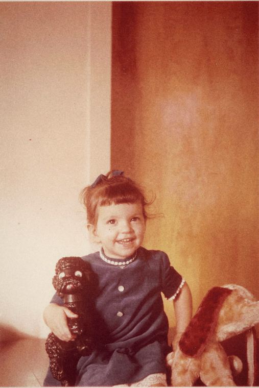 Josée enfant, en robe marine à col blanc, un jouet dans les mains.